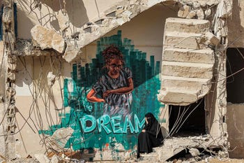Una donna siede lungo i gradini rotti di un edificio parzialmente crollato distrutto dai bombardamenti durante il conflitto del maggio 2021 tra Hamas e Israele, accanto a un murale di graffiti raffigurante una ragazza e una didascalia con la scritta "I've dream", a Gaza City ad agosto .