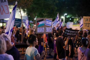 An Israeli protester holds a sign with the Palestinian and Israeli flags, with the word 'People' between them and below them 'We are brothers,' at a demonstration against the judicial coup in Tel Aviv, August 2023.