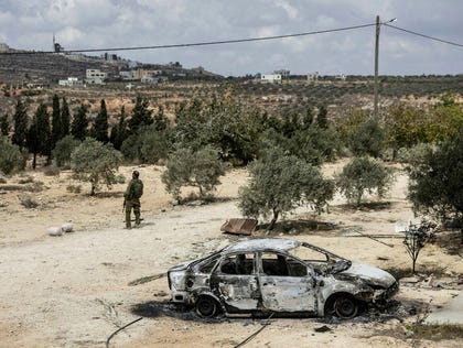IDF soldier stands next to a burnt car in Jalud, Tuesday.