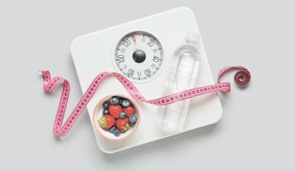 Weight scales with measuring tape, bottle of water and fresh berries on grey background. Slimming concept